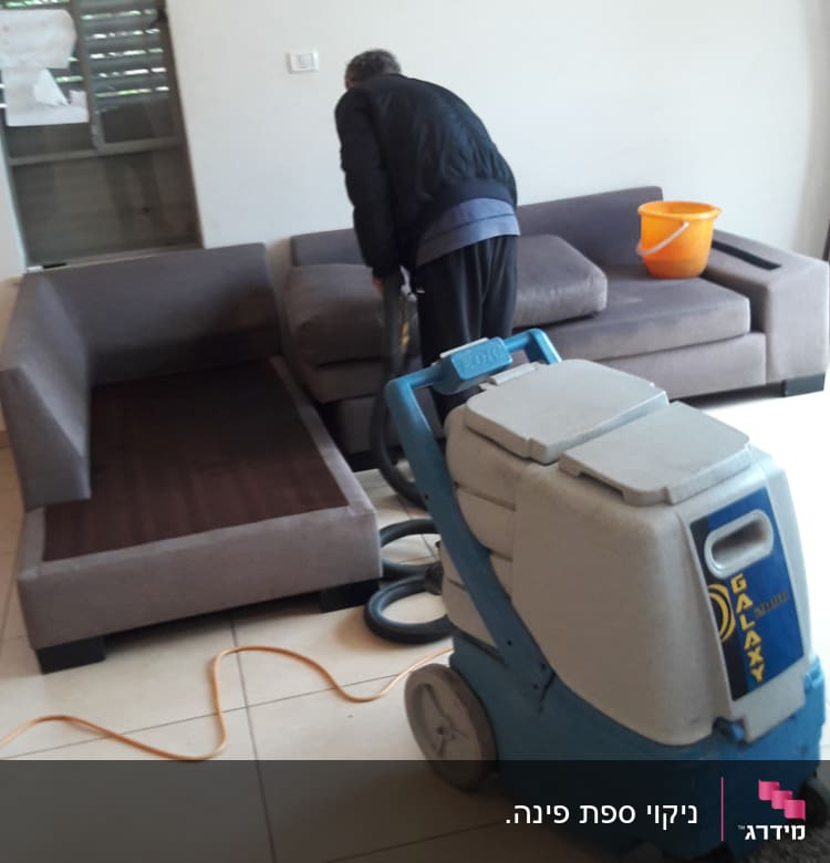 אדם מנקה ספה עם מכונת ניקוי מקצועית